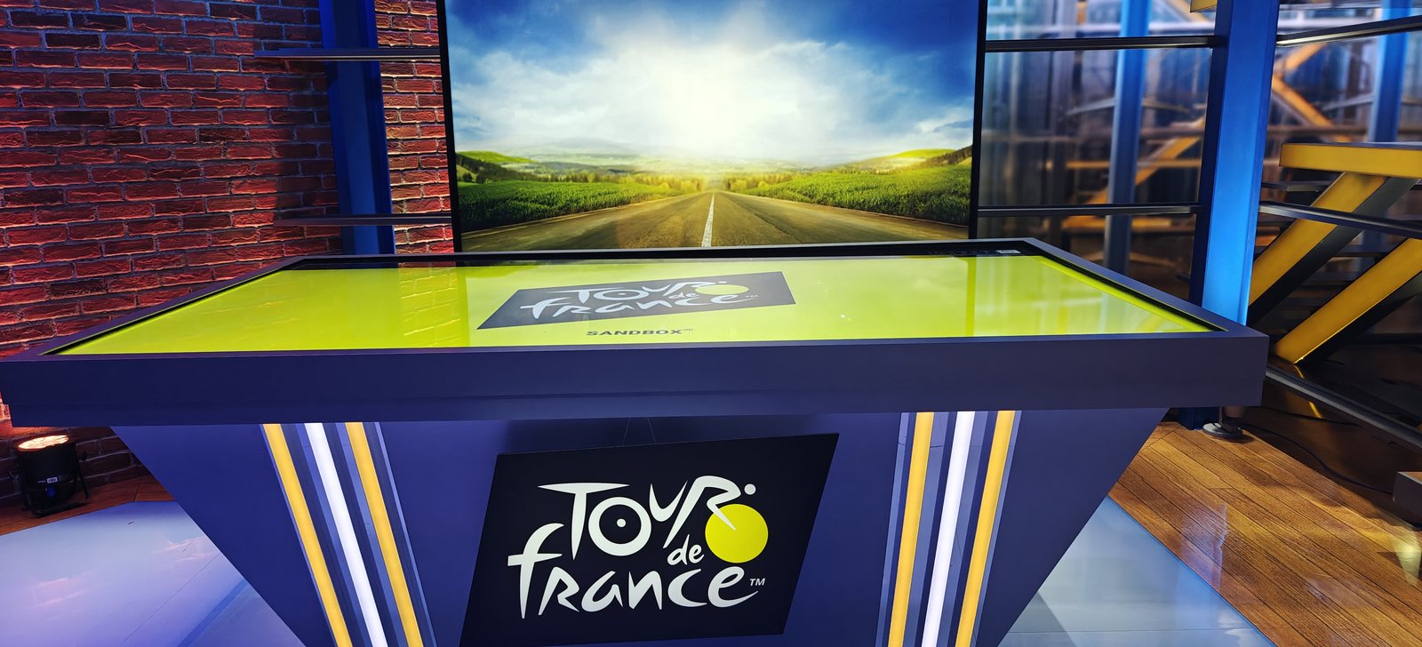 The Sandbox AR touch-table in NBC's studio, branded Sandbox × Tour de France, with the open-road backdrop